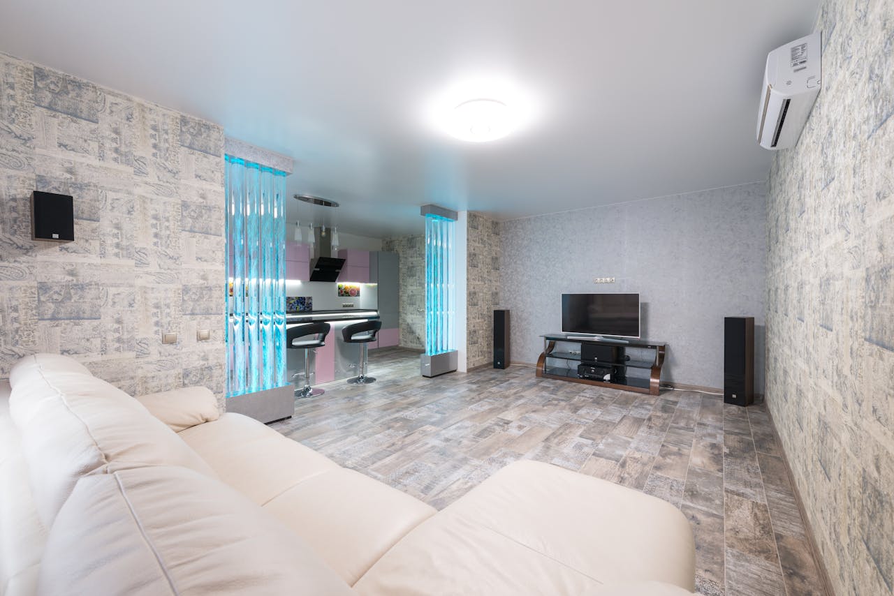 services-03 Comfortable white sofa placed in spacious room with TV and decorative colorful bubble wall near modern kitchen in stylish apartment
