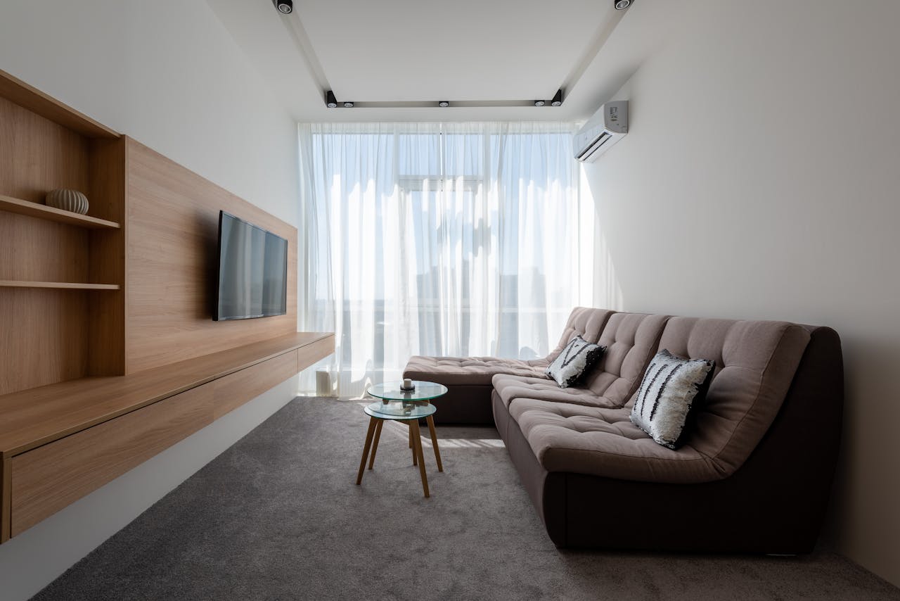 gallery-2 Comfortable couch with cushions near side tables against wall with wooden cupboard and modern TV in stylish living room with window