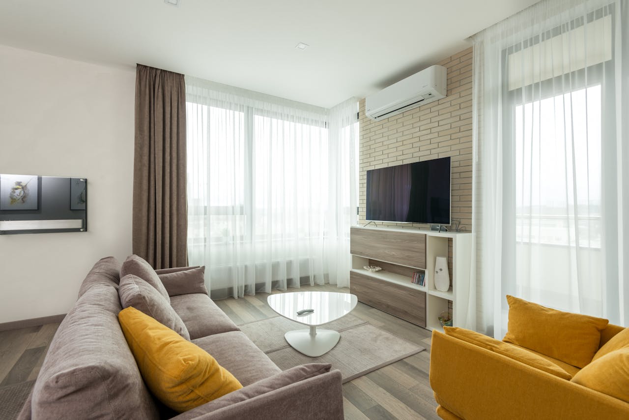 hero-img-02 Soft comfortable sofa with cushions and armchair placed in front of TV hanging on brick wall in spacious living room of modern apartment