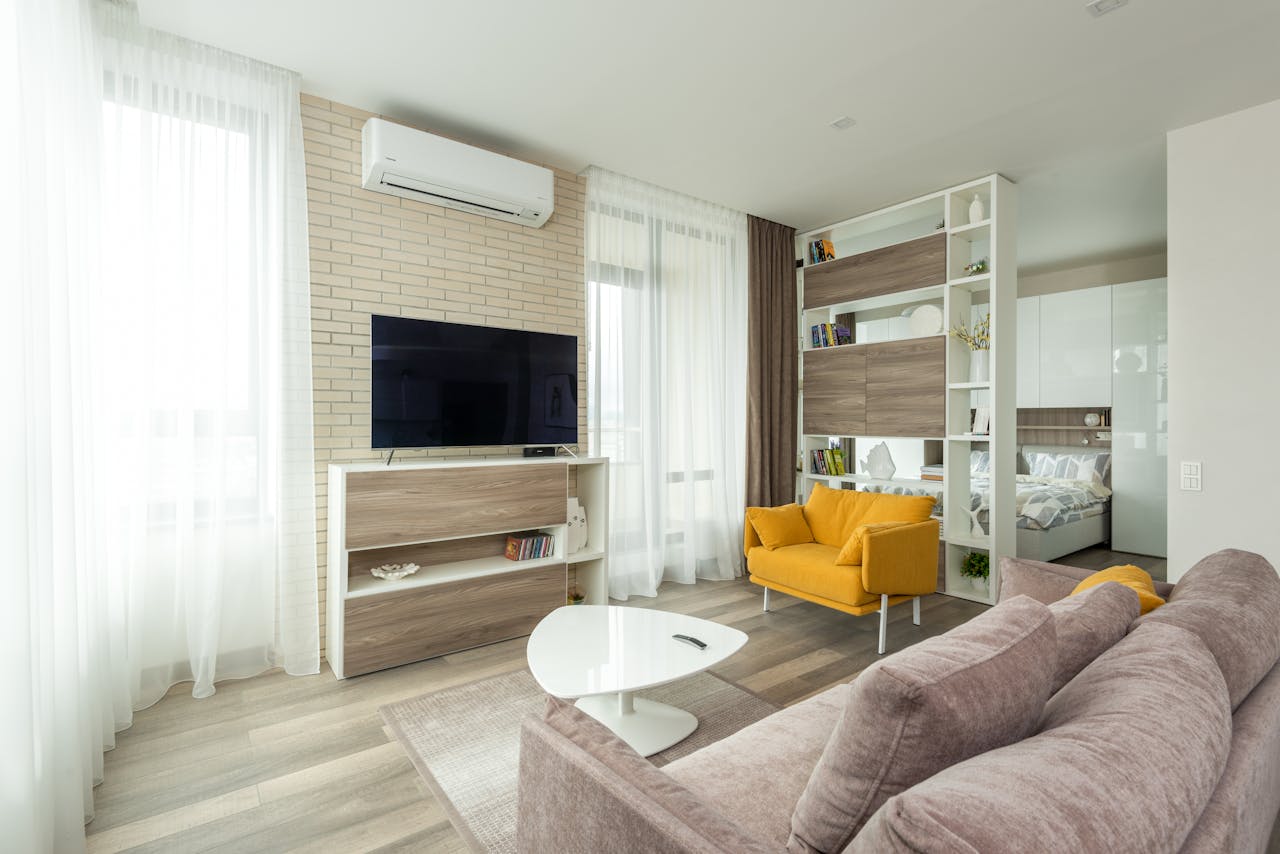why-choose-us Cozy sofa and armchair placed near cabinet with TV set in contemporary living room separated from bedroom with cupboard and shelves in spacious studio apartment
