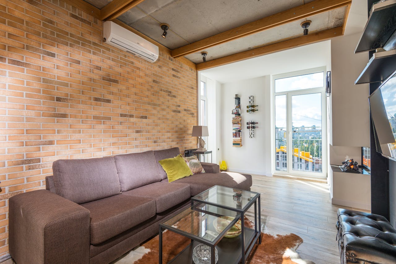 services-02 Bright living room with contemporary design, featuring a brown sofa and brick wall.